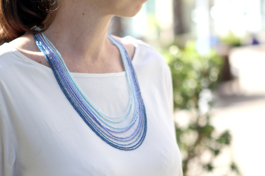 Andrea wearing a white shirt and the completed ombre blue multi-strand seed bead necklace