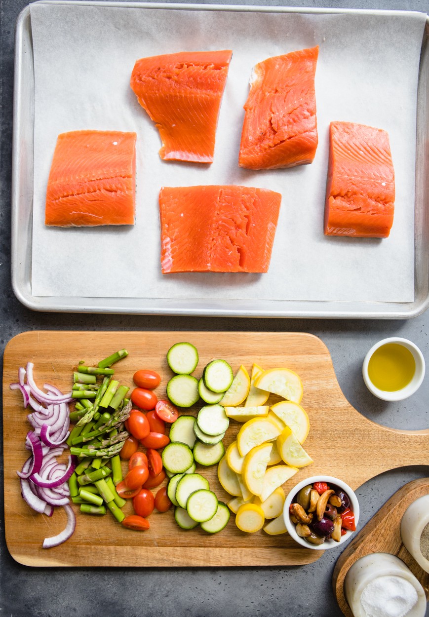 uncooked salmon filets on a baking sheet next to uncooked chopped vegetables