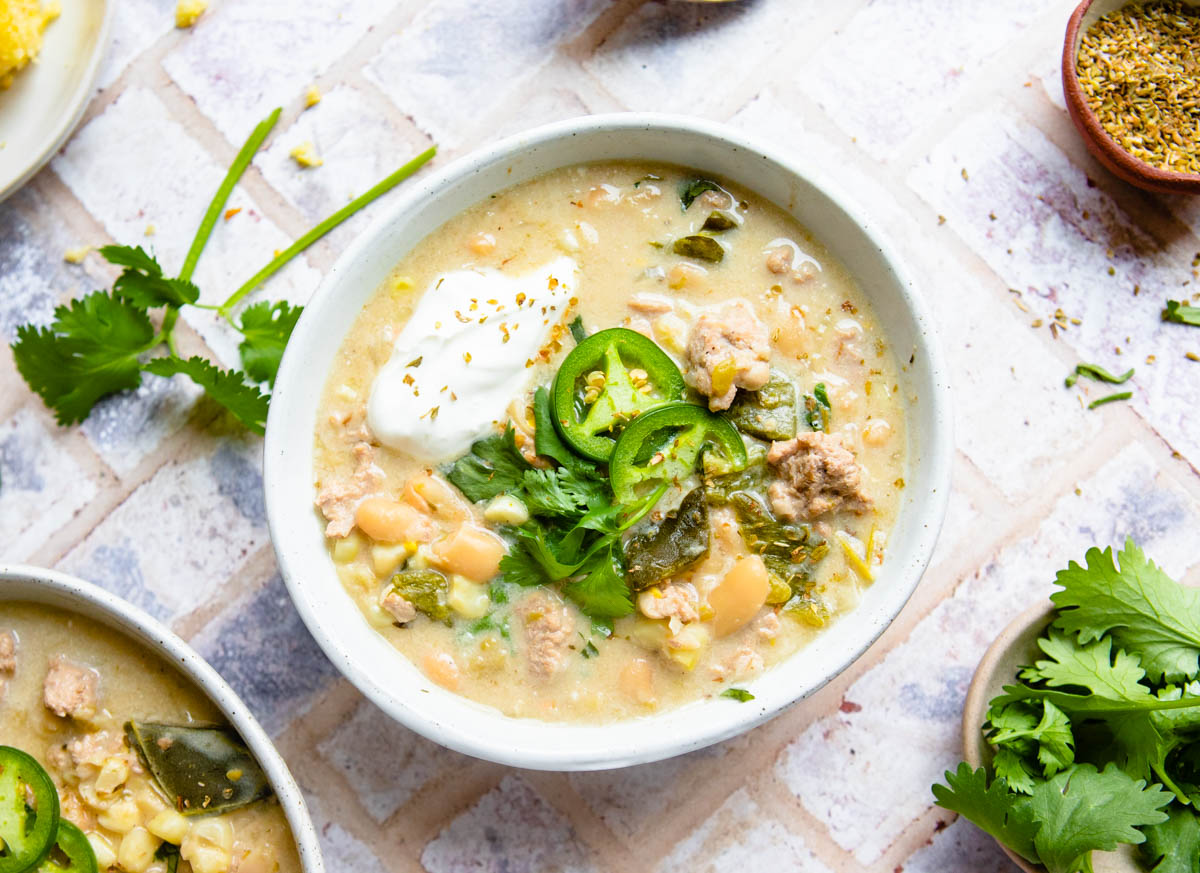 a white ceramic bowl filled with instant pot white bean chicken chili and garnished with jalapenos and cilantro and sour cream