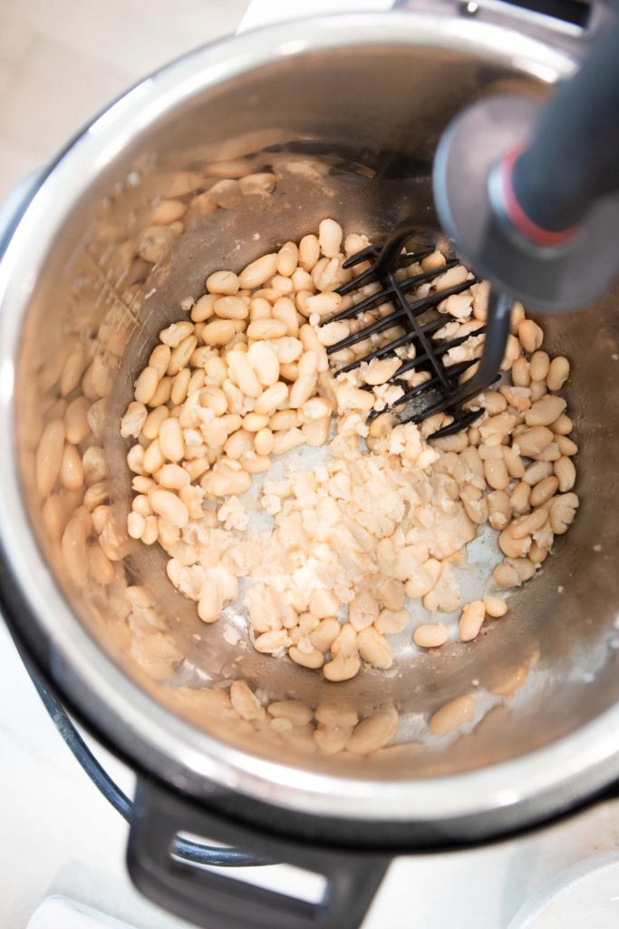 white beans being smashed up in the bowl of an Instant Pot