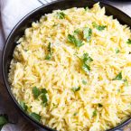 Large serving bowl of instant pot orzo with parsley garnished on top.