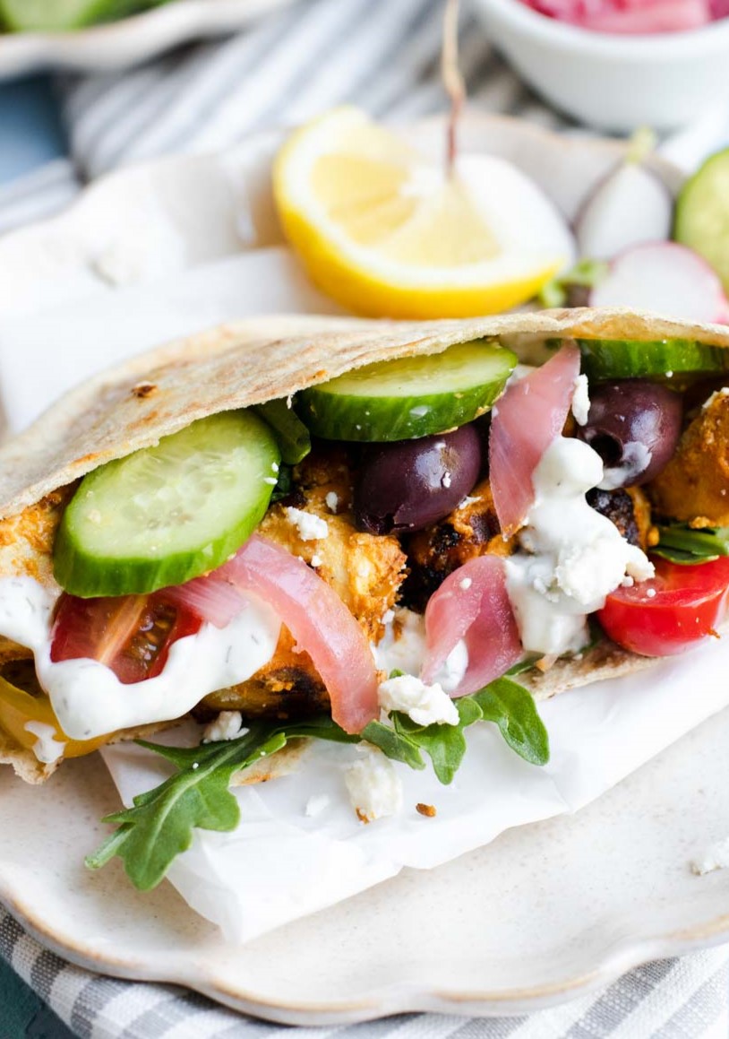 chicken pita shawarma garnished with cucumbers, tomatoes, pickled onions and olives on a plate with a lemon slice