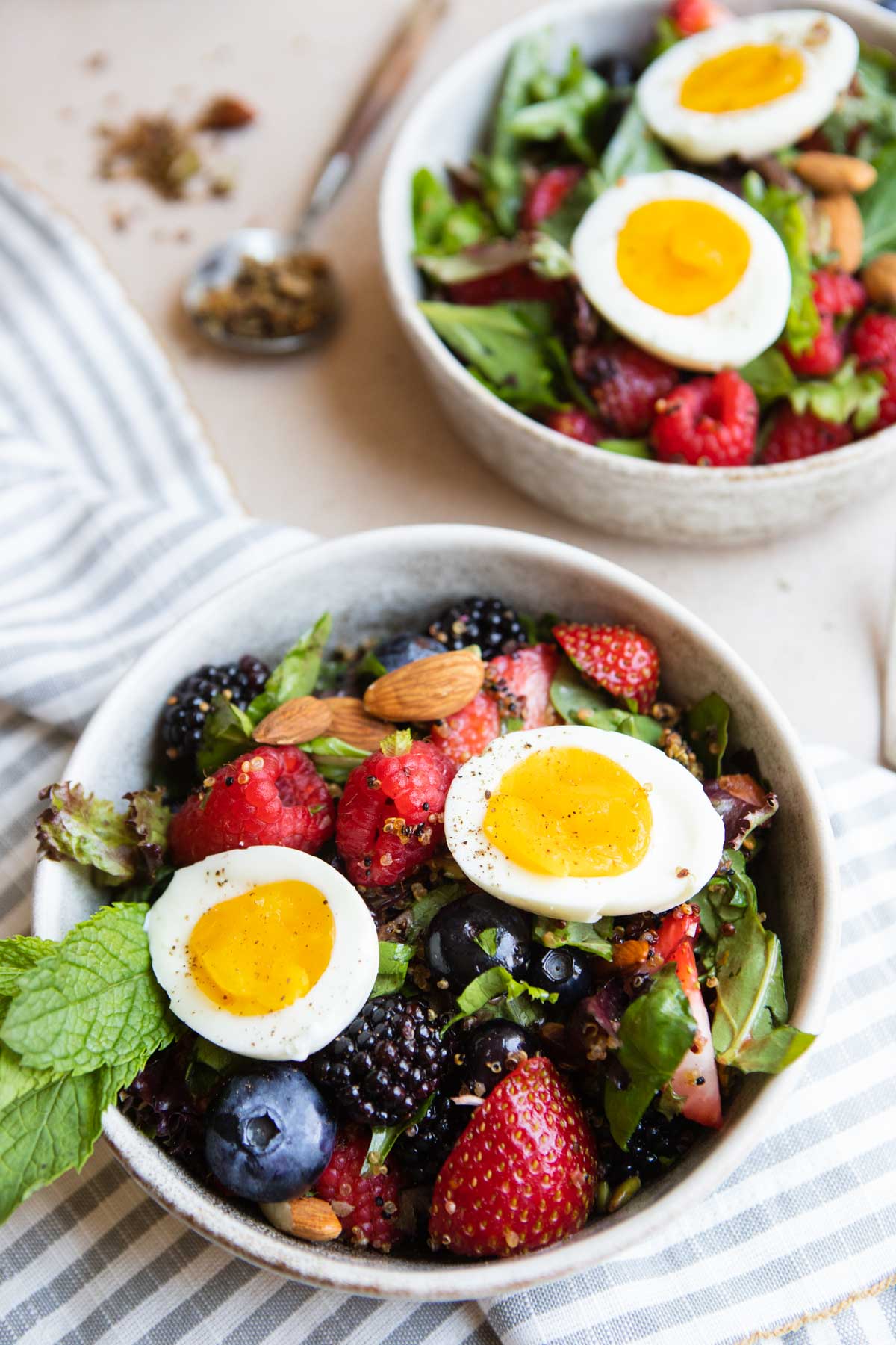 2 bowls filled with a berry breakfast salad topped with a medium boiled egg