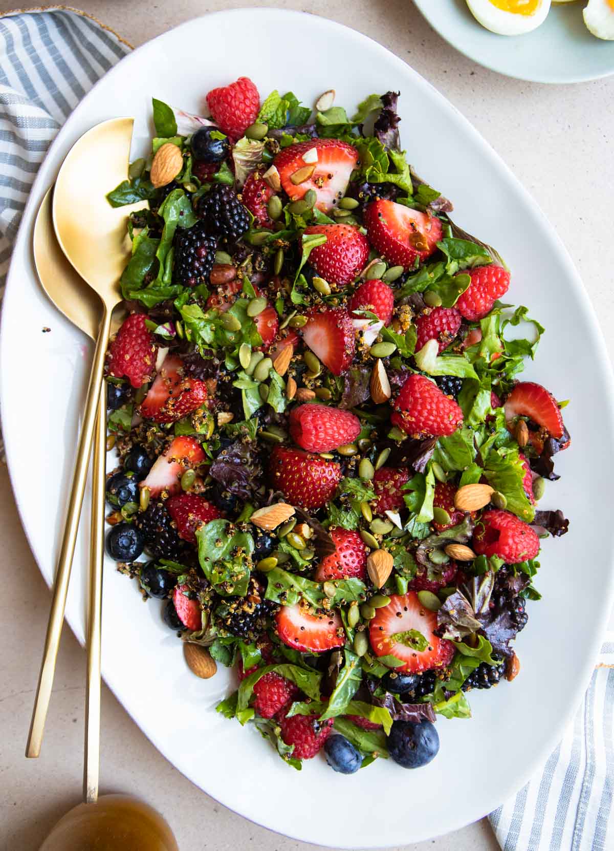 white platter and gold serving tongs with a berry salad on top