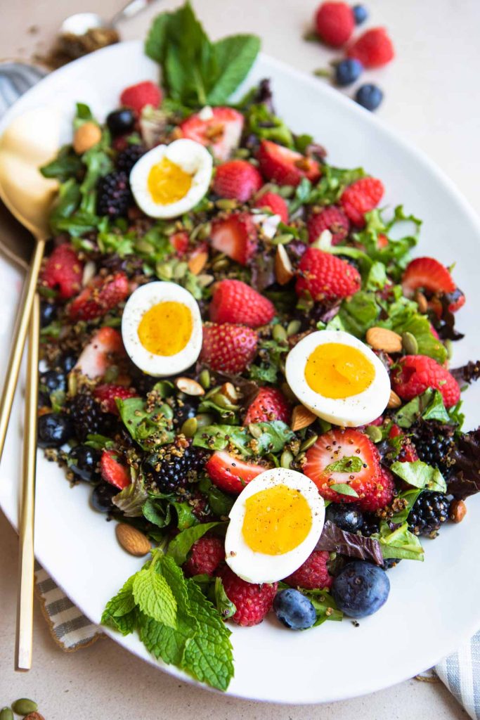 berry breakfast salad on a platter with gold serving tongs