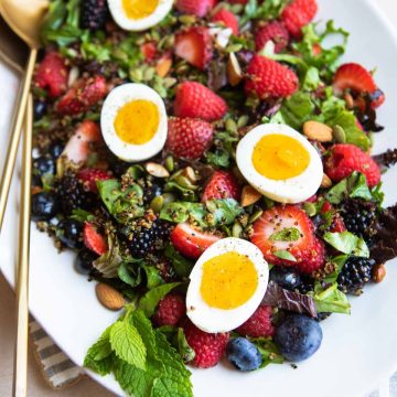 berry breakfast salad with soft boiled eggs on top served on a white platter