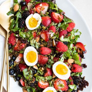 a large white platter filled with a breakfast salad and topped with hard boiled eggs and nuts