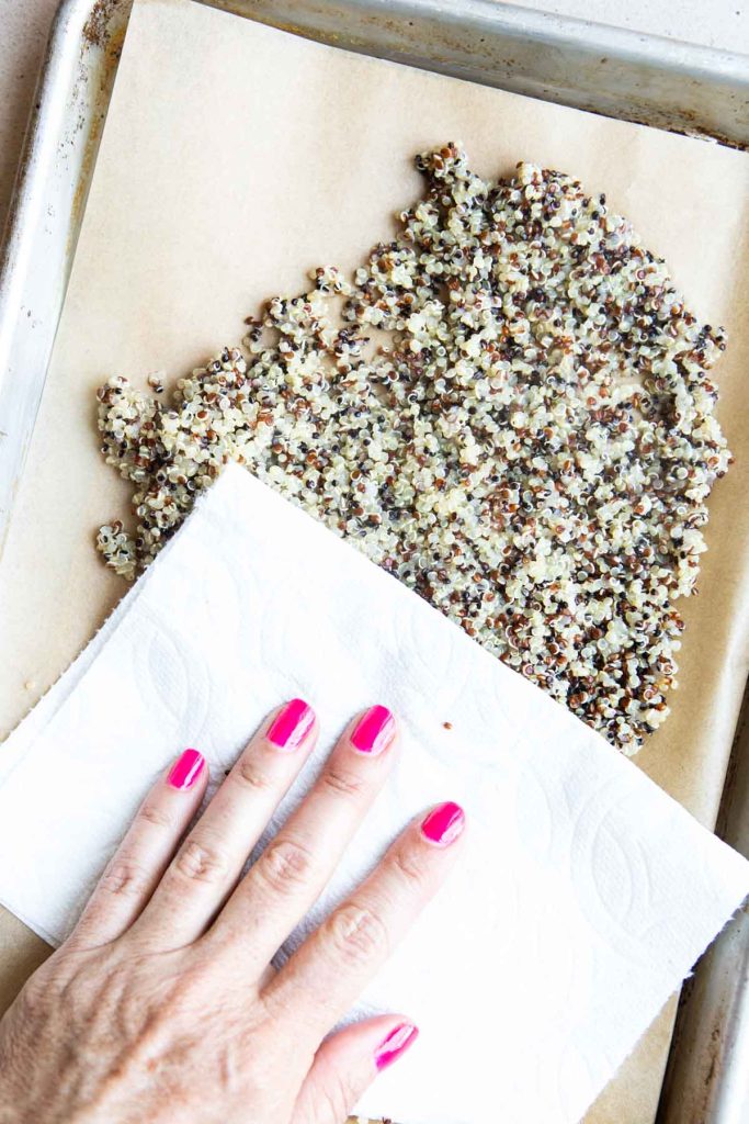 woman patting dry cooked quinoa on a baking sheet