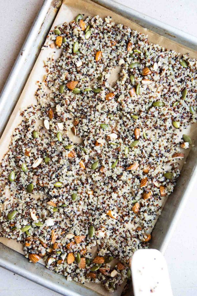 unbaked cooked quinoa and nuts on a rimmed baking sheet