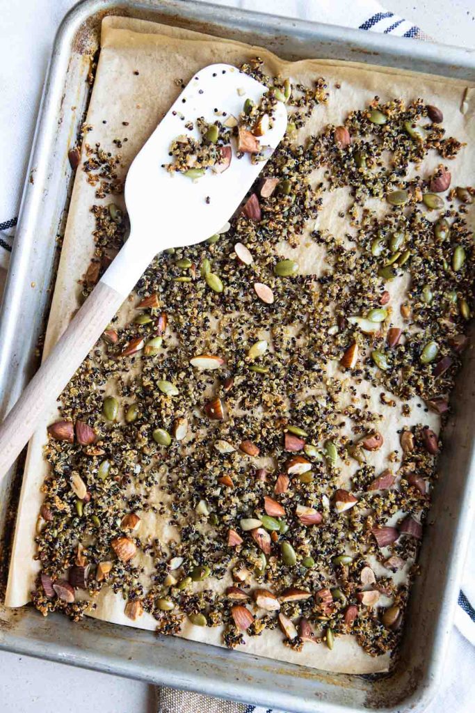 baked nutty quinoa on a parchment lined baking sheet and a silicone spatula