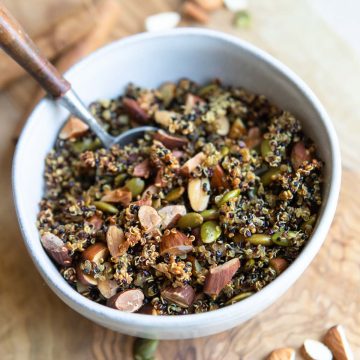 a wood cutting board sprinkled with nuts and seeds and a bowl filled with cooked crispy nutty quinoa