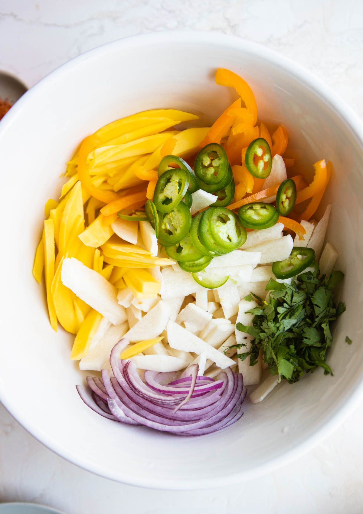 sliced fresh salad ingredients tossed in a white serving bowl