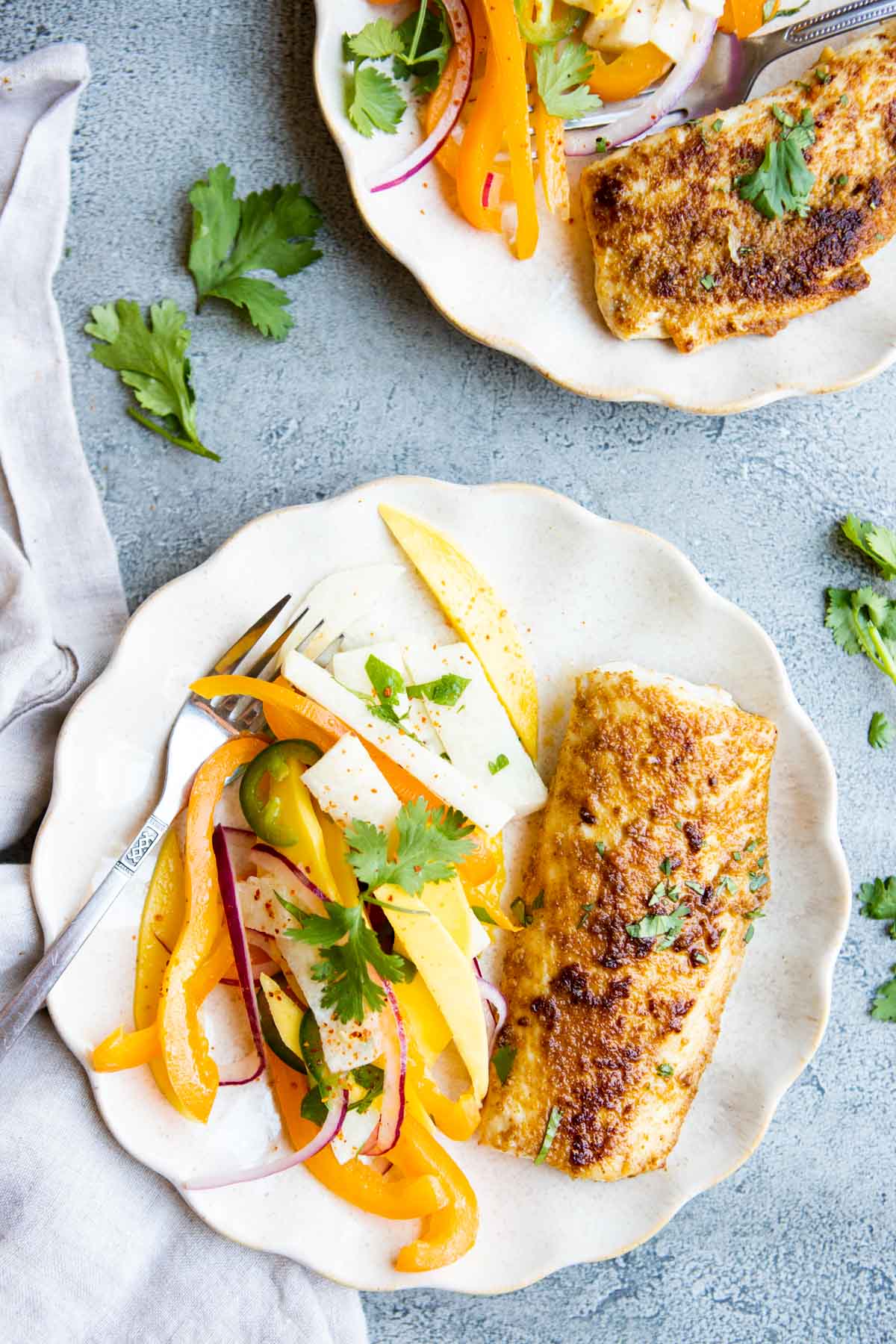 a scalloped plate with a piece of cooked mahi mahi and jicama mango salad