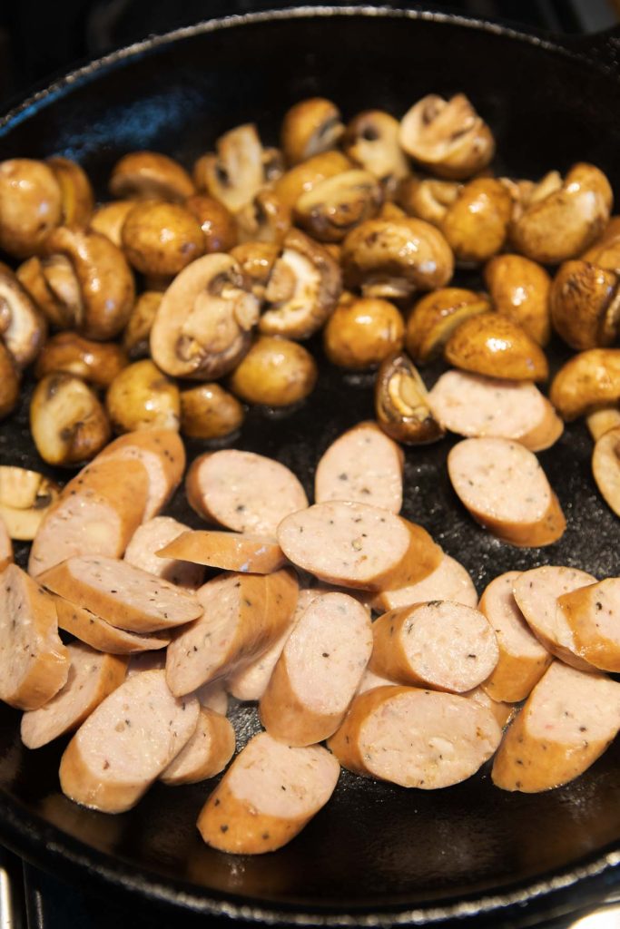 chicken sausage slices and mushrooms cooking in a cast iron skillet