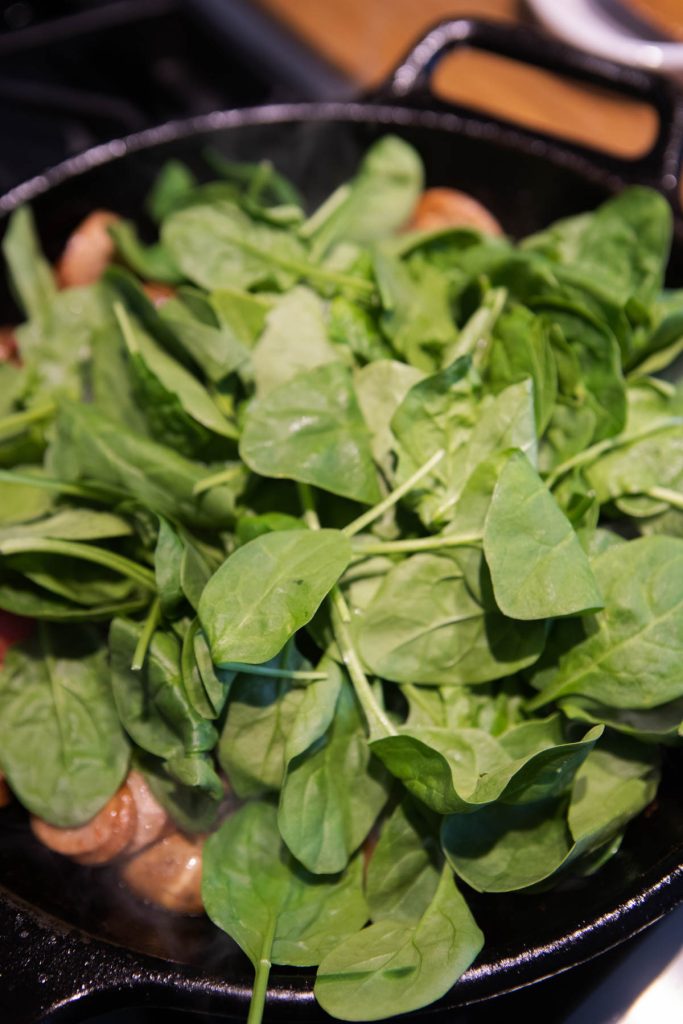 raw spinach added to a cast iron skillet