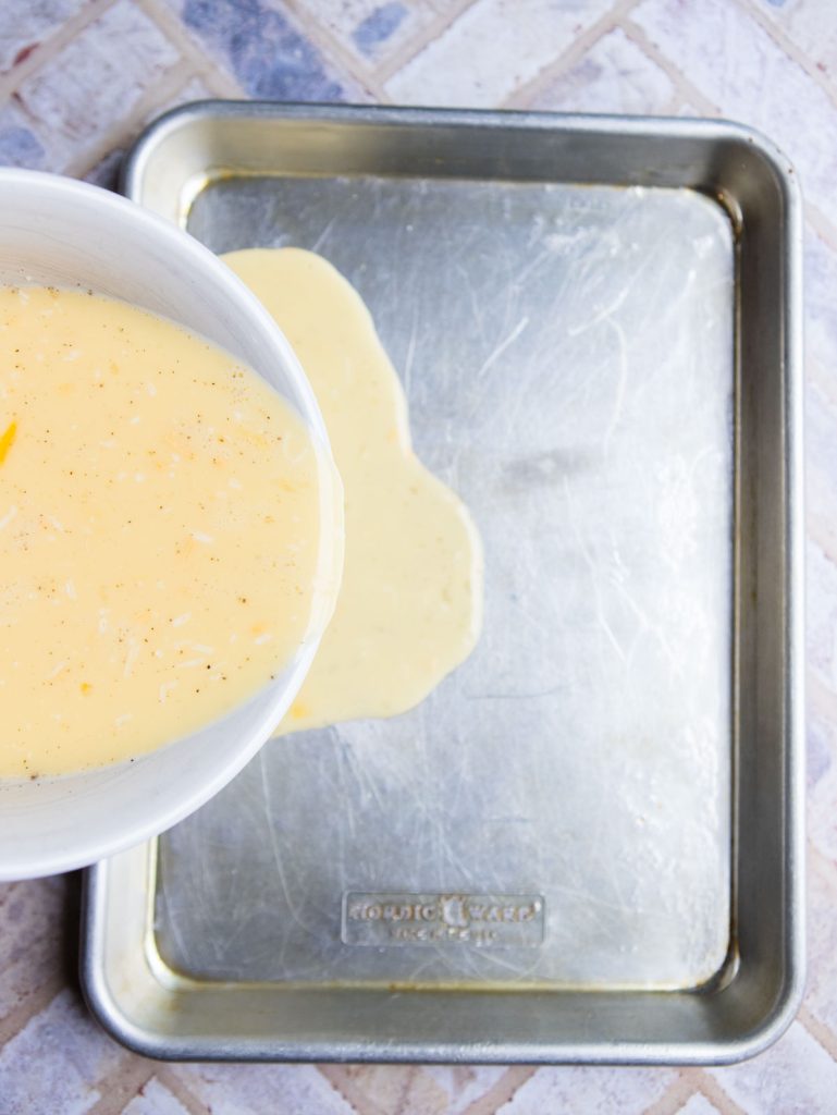 scrambled eggs being poured into a rimmed baking sheet