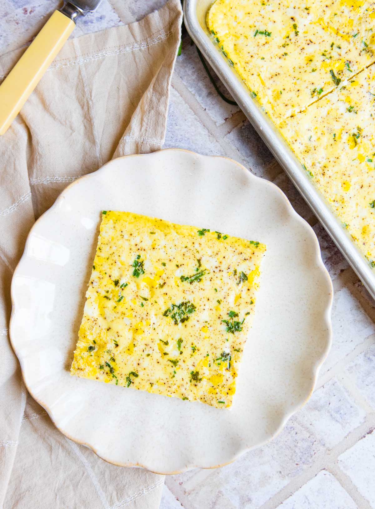 A square of sheet pan eggs served on a white scalloped plate