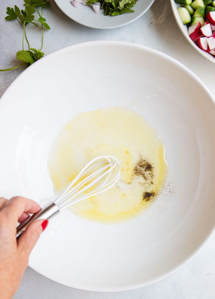 honey lemon vinaigrette being whisked in a large white serving bowl