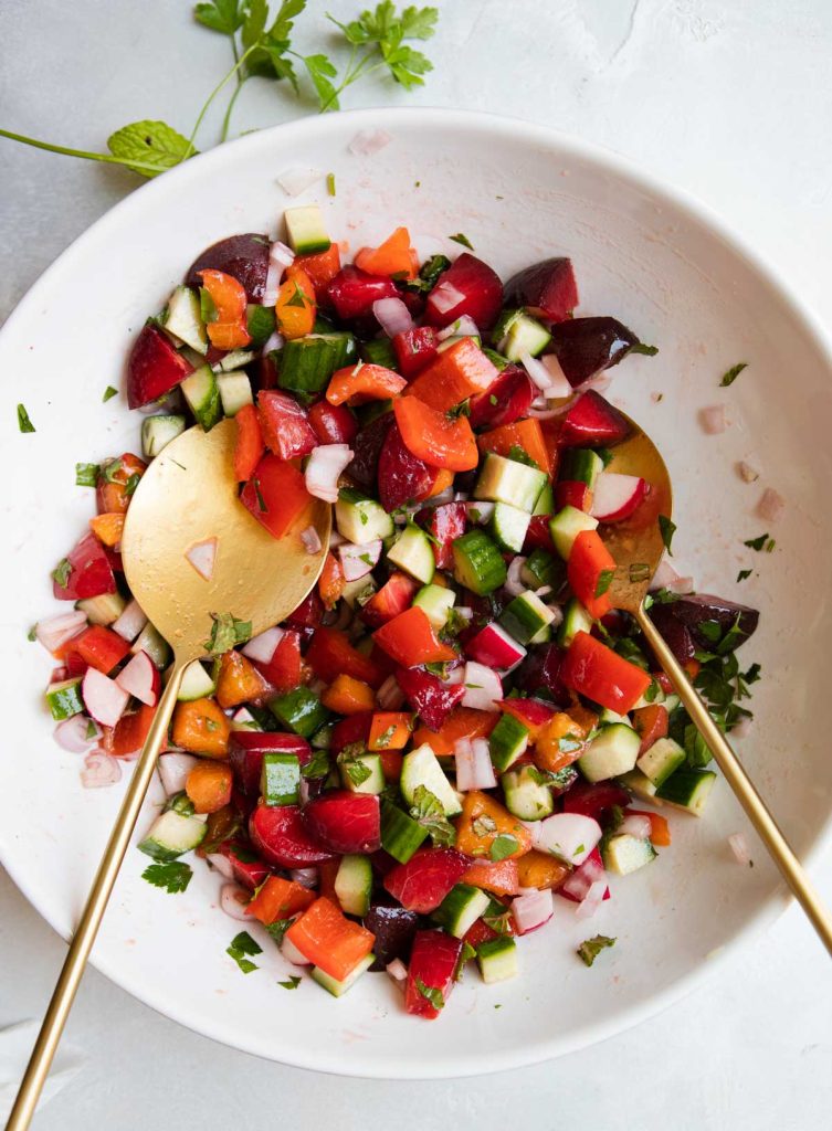 large white bowl with the ingredients to make a stone fruit salad including plums, apricots. cucumber, red bell peppers and radishes