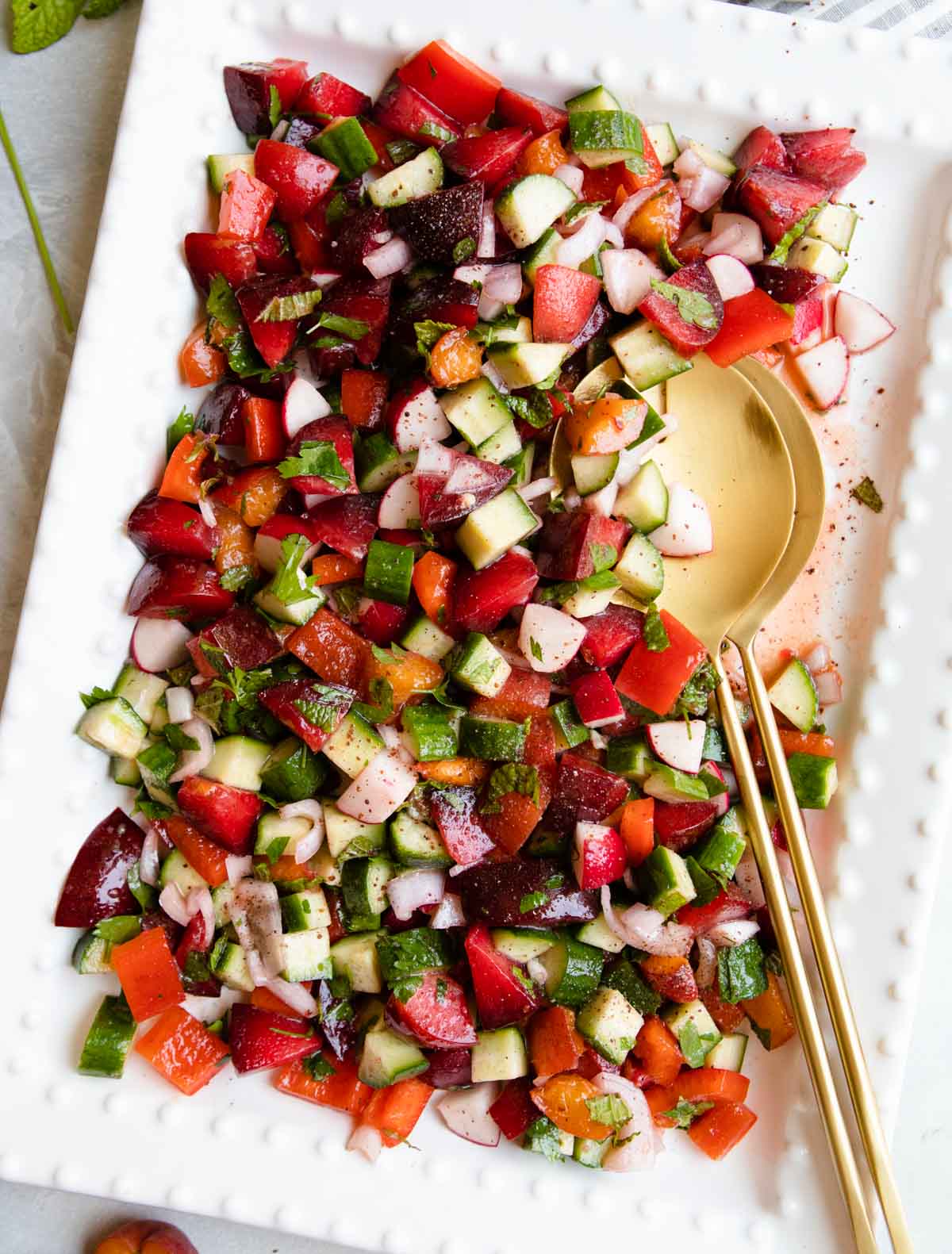 fruit and veggie summer salad served on a large white ceramic platter with gold tongs