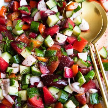 stone fruit salad with radishes, peppers and cucumbers tossed in a lemon vinaigrette served on a white platter with gold tongs