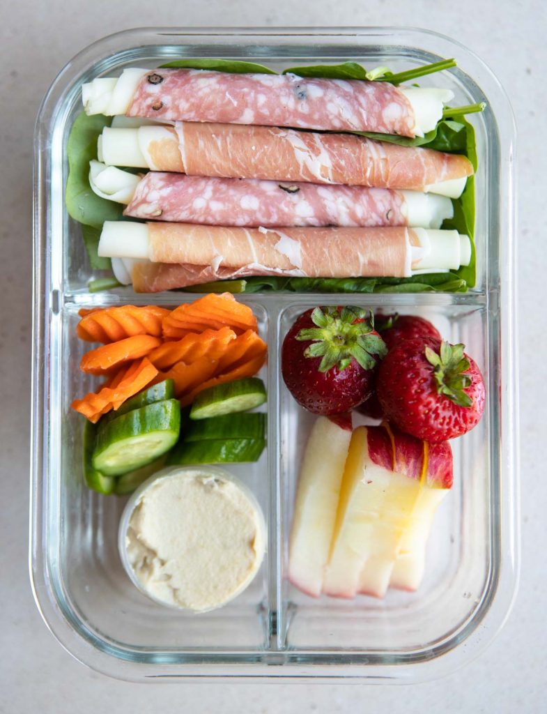 cold cuts and provolone with apples, strawberries, cucumbers and carrots in a glass meal prep container 