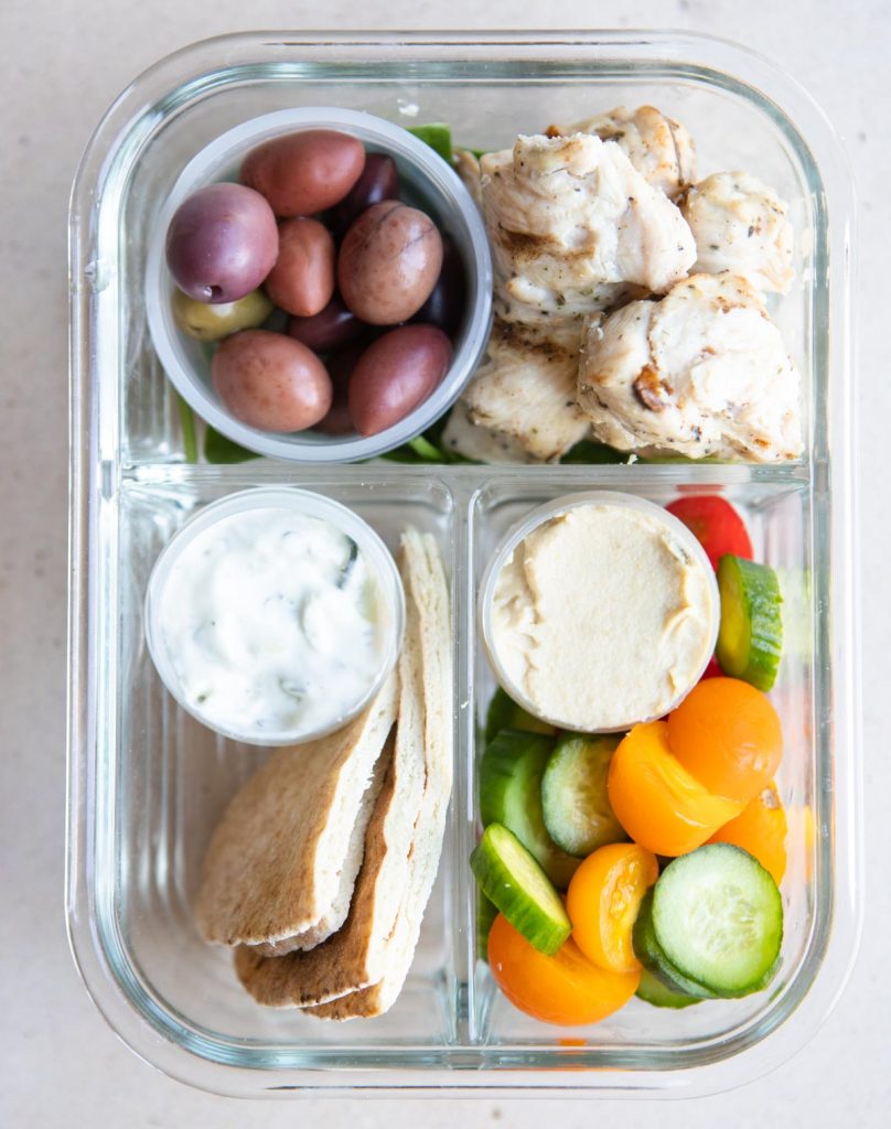 grilled chicken, pita, fresh veggies, hummus and olives in a glass meal prep container