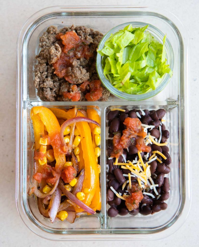 ground beef, grilled veggies and black beans in a glass meal prep container 