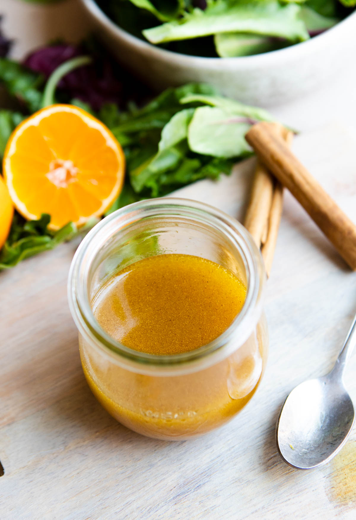 a glass jar filled with orange dressing and placed next to a spoon and salad greens