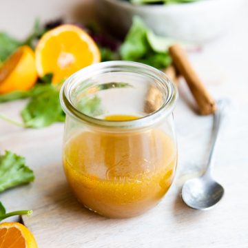 orange vinaigrette in a small glass jar next to a spoon and salad greens