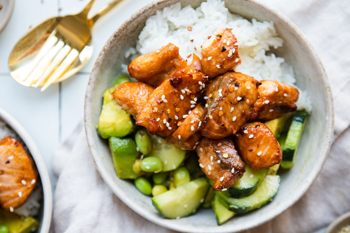 a beige bowl filled with white rice, a cucumber salad and air fryer teriyaki salmon 