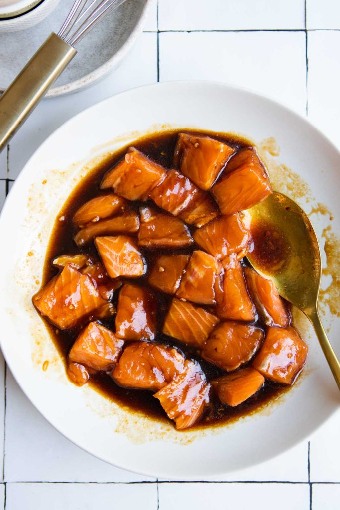 raw salmon bites marinating in a semi-homemade teriyaki marinade in a shallow white bowl