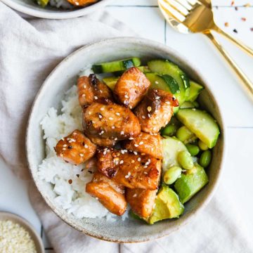 teriyaki salmon bites on top of a bed of white rice and cucumber edamame salad