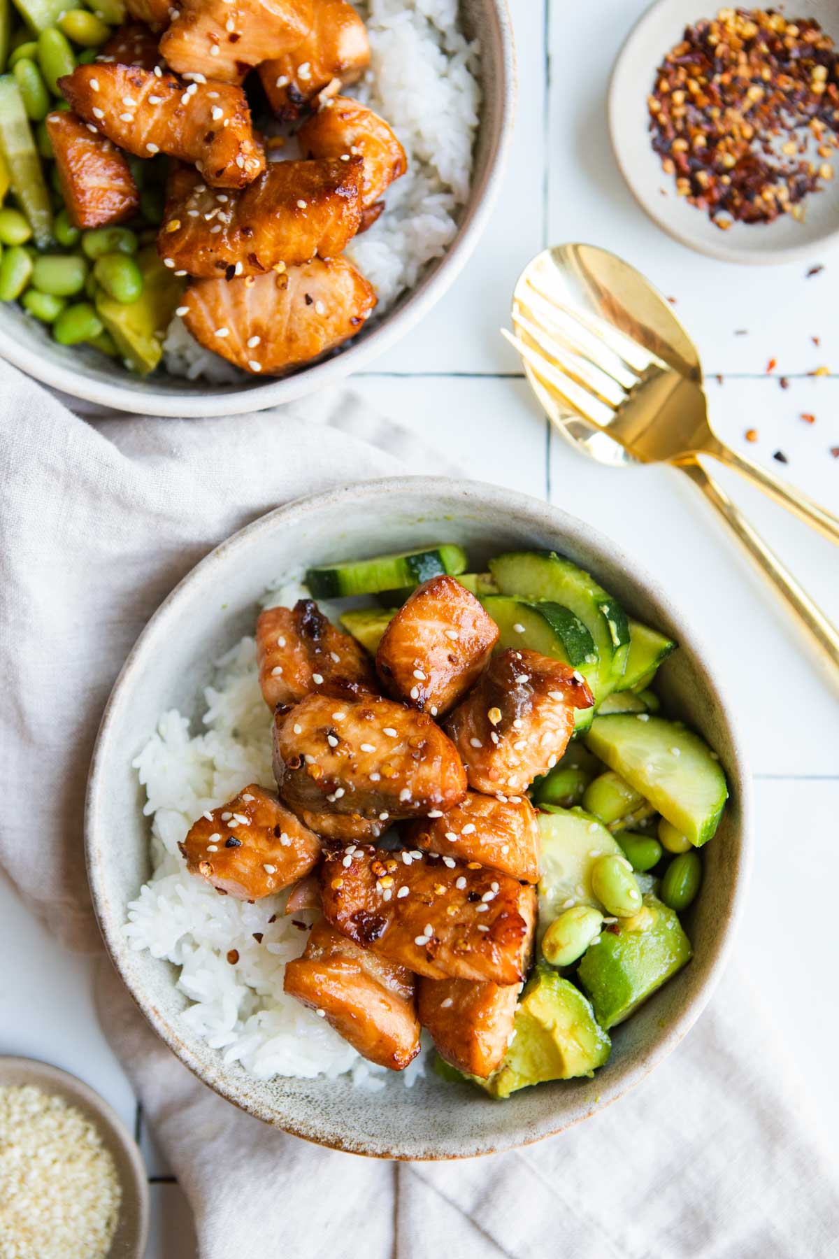 2 beige bowls fille with rice, cucumber and edamame salad and topped with air fryer teriyaki salmon