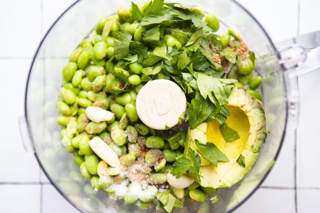 fresh parsley, avocado, garlic, edamame and spices in the bowl of a food processor