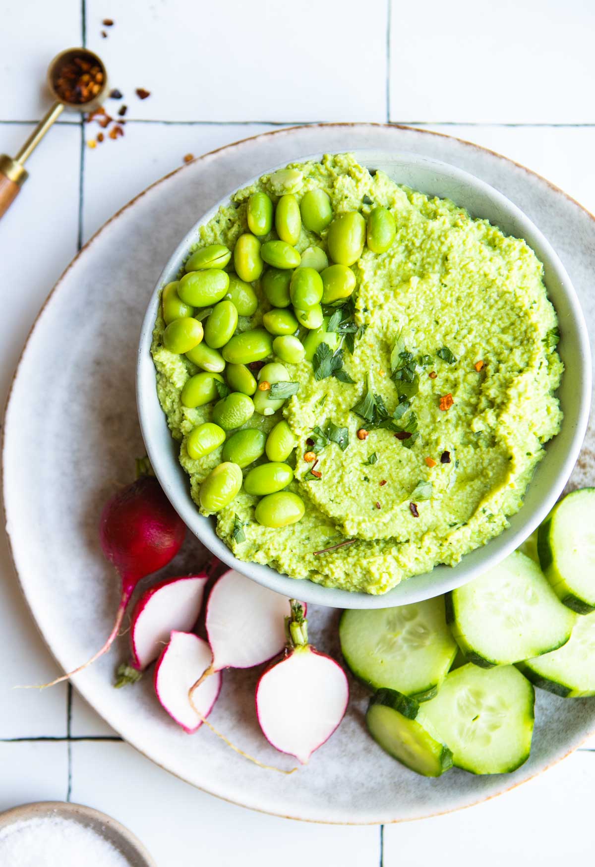 beige plate with cut up veggies on it and a gray bowl filled with edamame hummus sitting on top of the plate