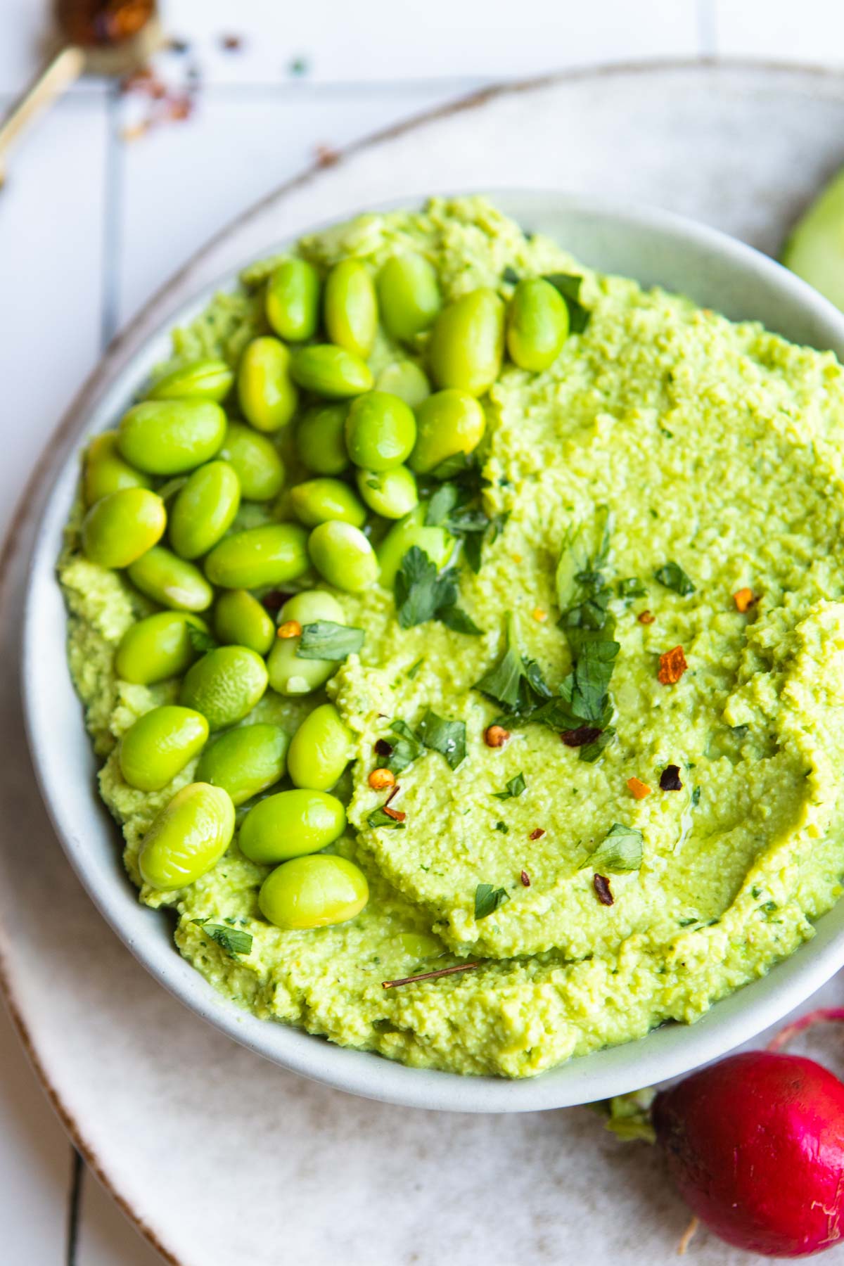 bowl filled with edamame and avocado hummus and garnished with whole edamame and red chili flakes