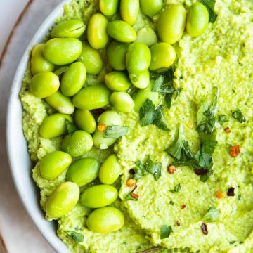 fresh shelled edamame garnished on top of a bowl filled with avocado and edamame hummus