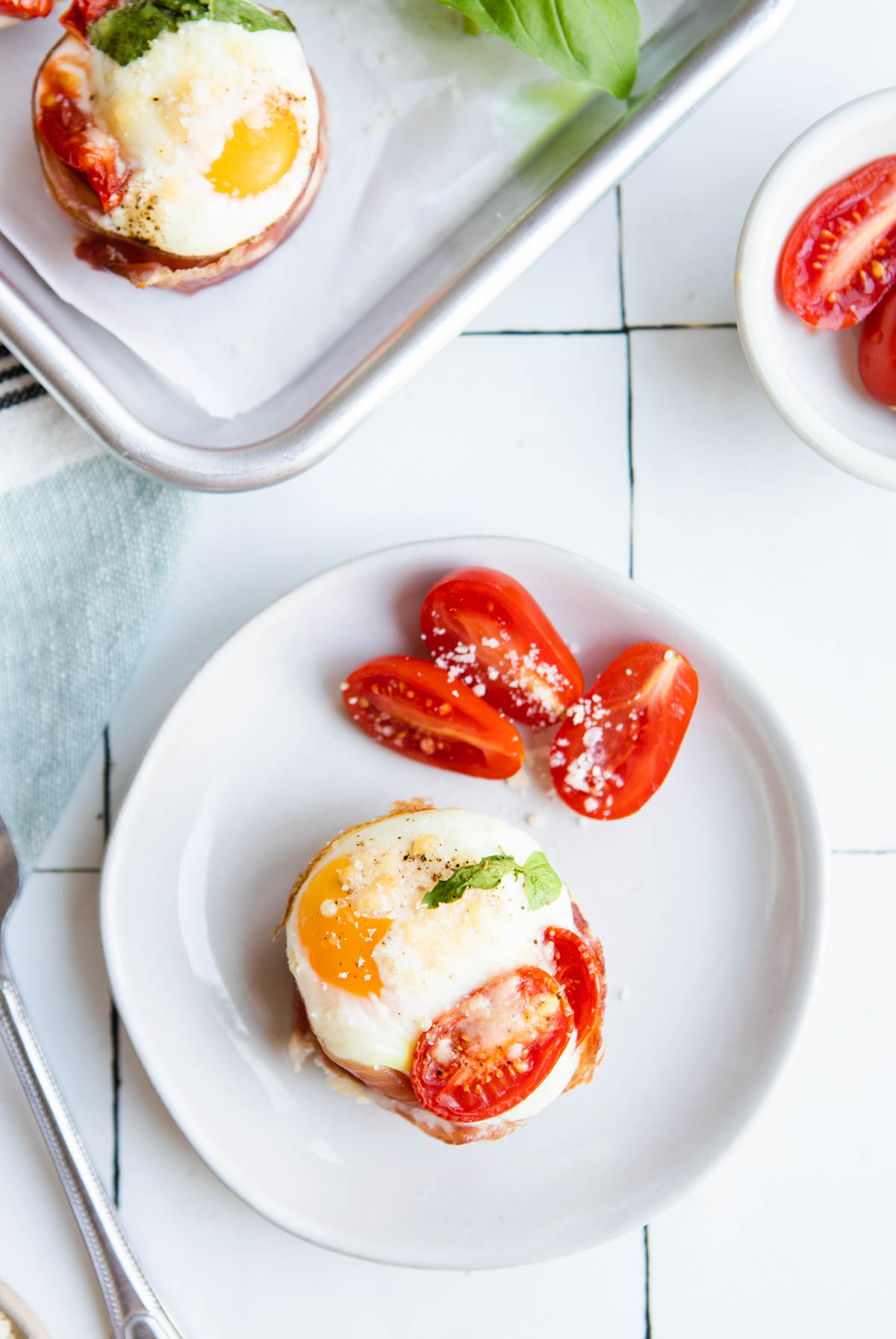 single prosciutto egg cup on a white plate with sliced cherry tomatoes 