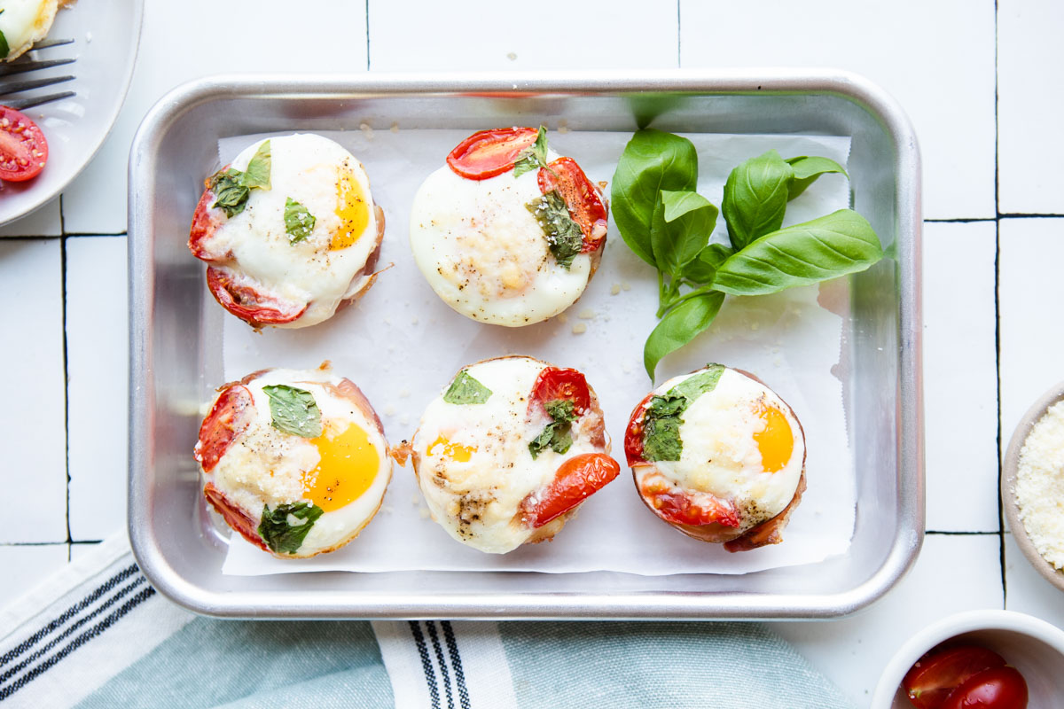 small sheet pan filled with 6 prosciutto egg cups garnished with basil