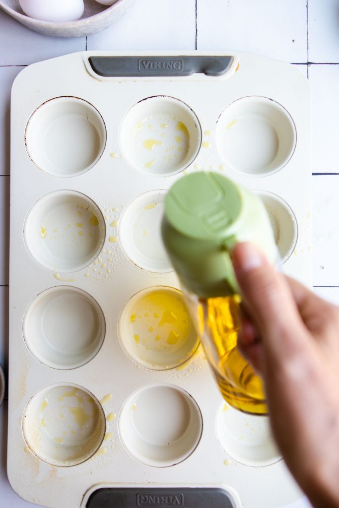 muffin tin being sprayed with cooking spray