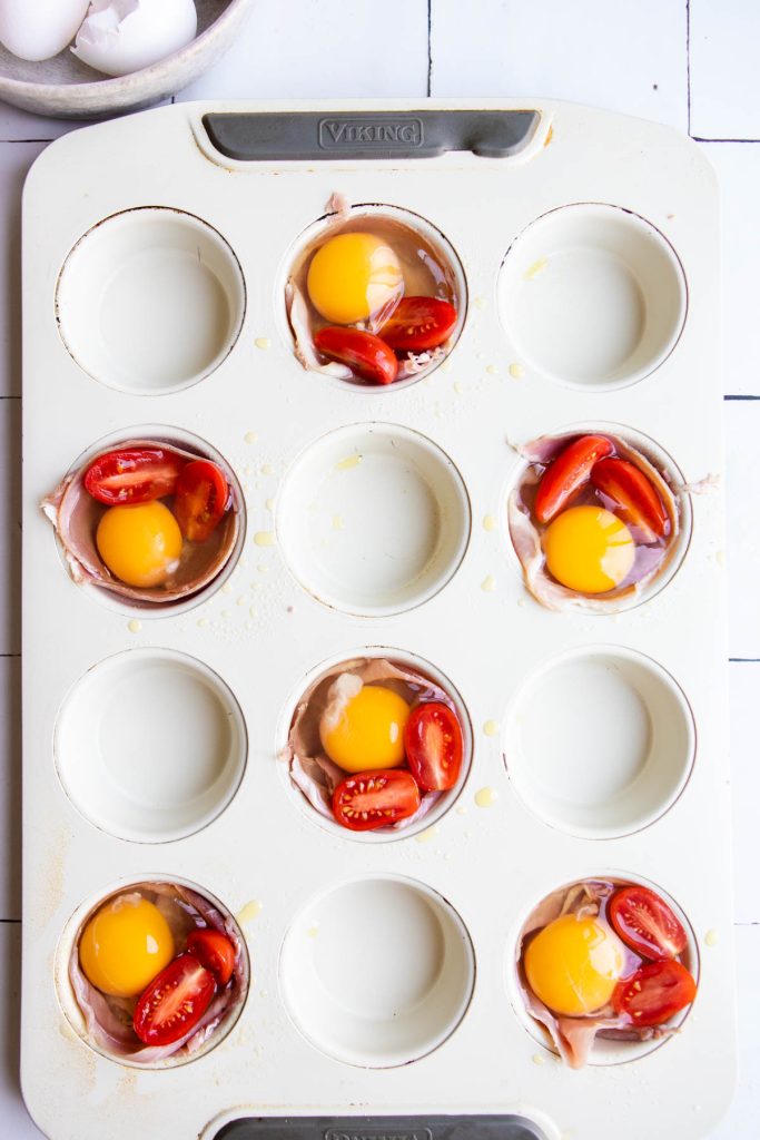 muffin tin filled with prosciutto a raw egg and cherry tomato slices