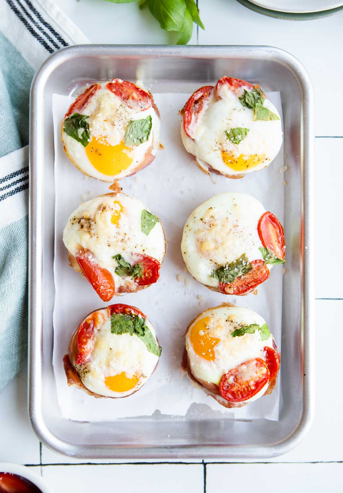 ⅛ sheet pan with 6 prosciutto egg cups with tomatoes and basil and garnished with parmesan cheese