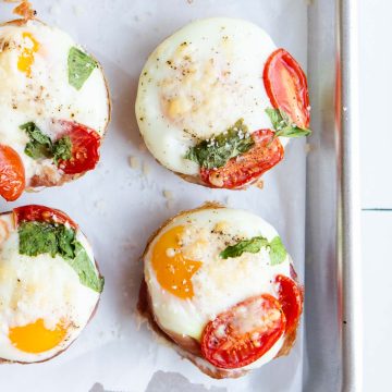 prosciutto egg cups garnished with basil and parmesan cheese on a metal rimmed sheet pan