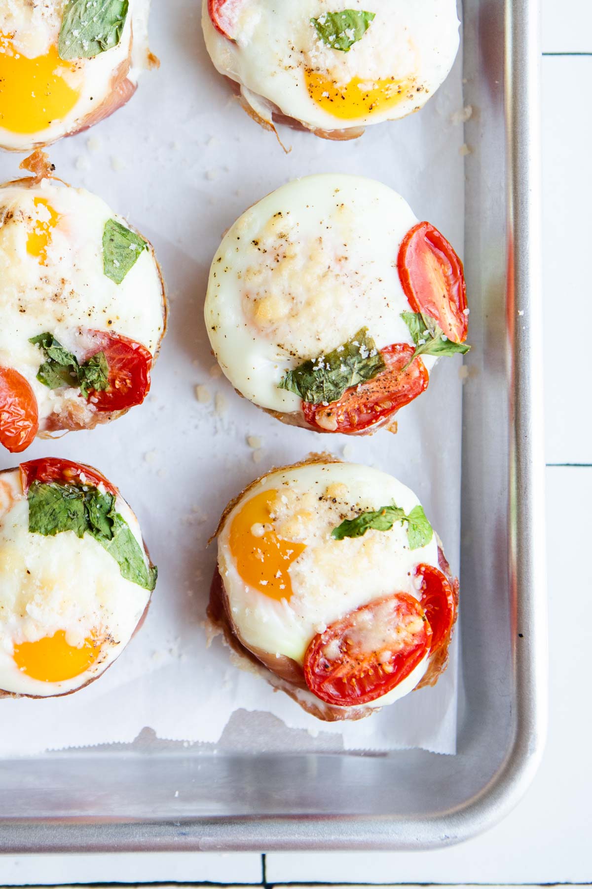 prosciutto egg cups garnished with basil and parmesan cheese on a metal rimmed sheet pan