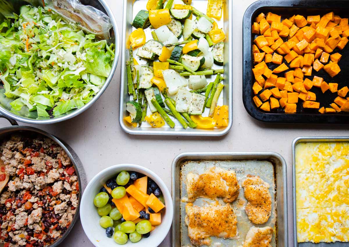 sheet pans and skillets filled with various veggies and proteins for meal prep 