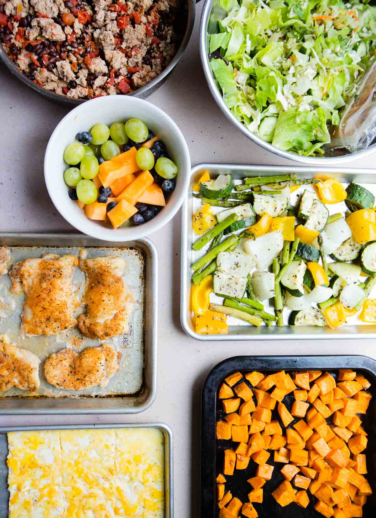 7 dishes filled with chicken eggs, veggies and salad greens to show how you can make easy high protein meal prep