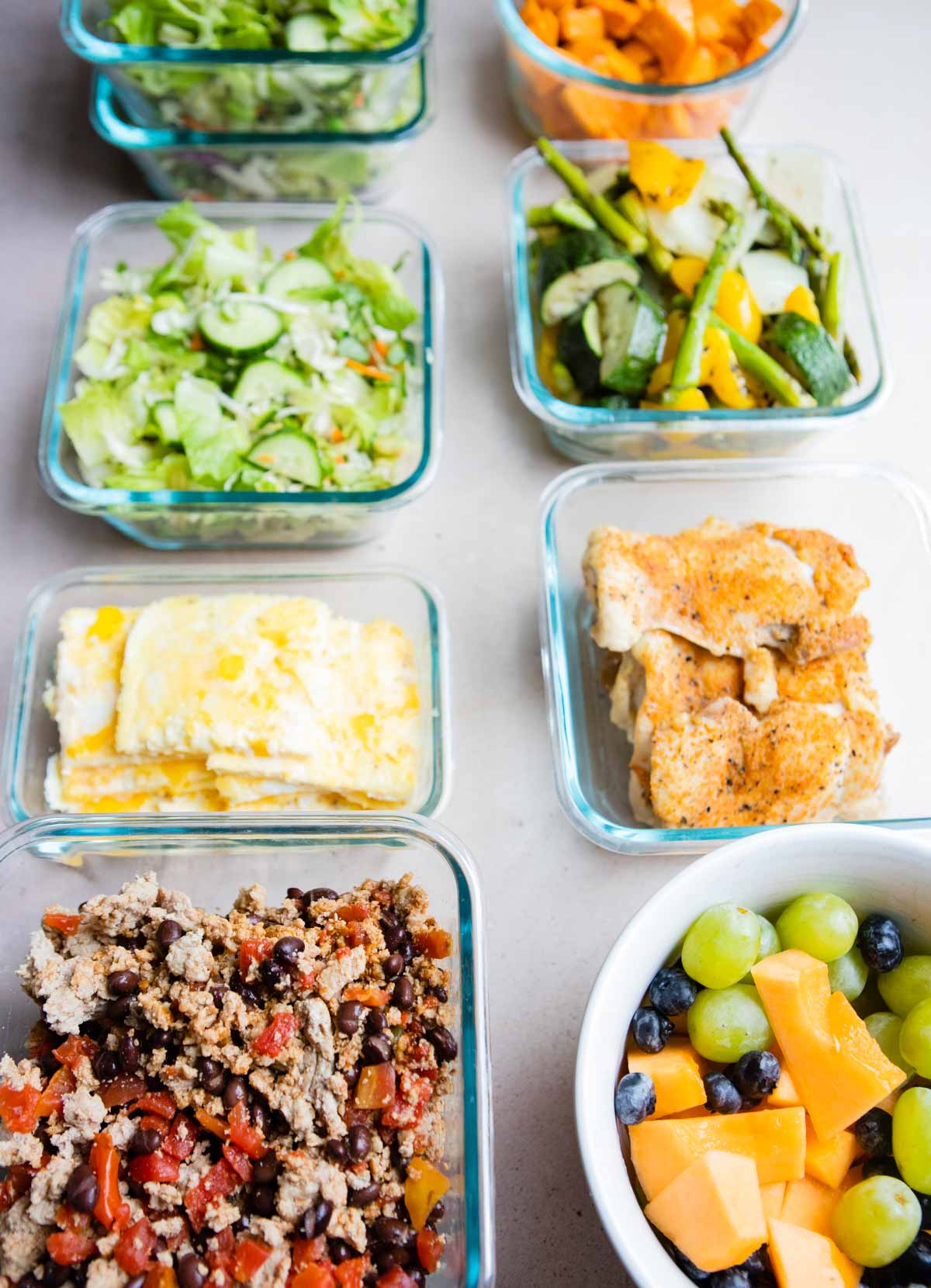 glass meal prep containers filled with various cooked foods and fresh fruit and veggies 