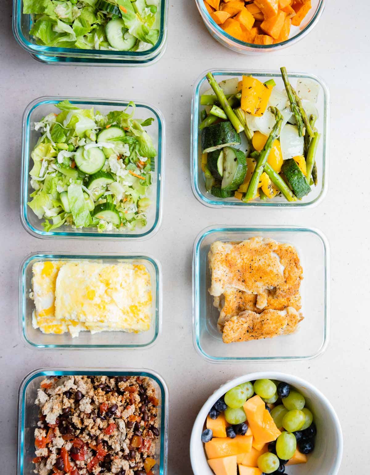 square glass containers filled with precooked veggies, fruit salad and easy high protein meal prep