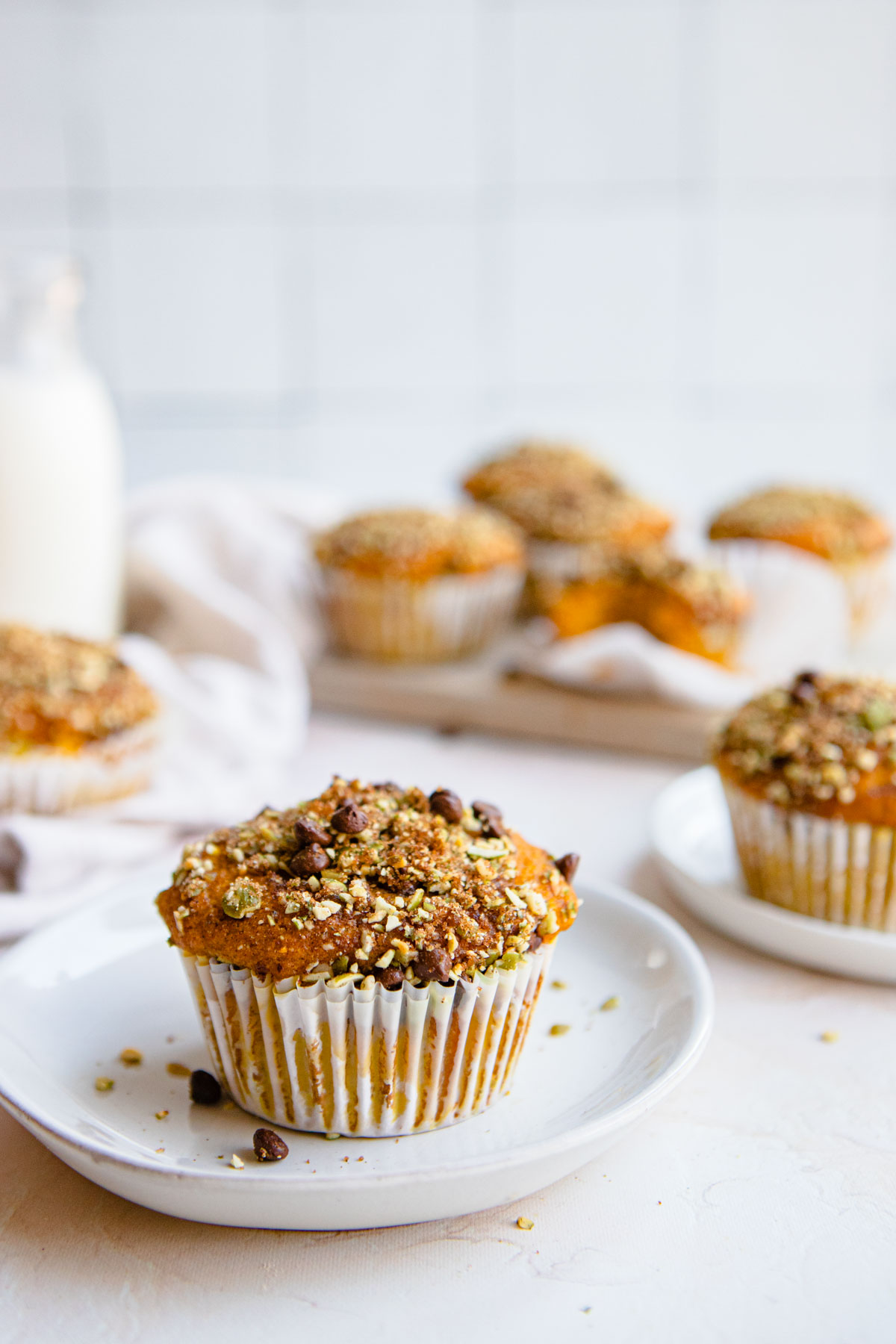 protein muffins pumpkin flavored topped with a pepita and dark chocolate streusel topping sitting on a stack of white plates 